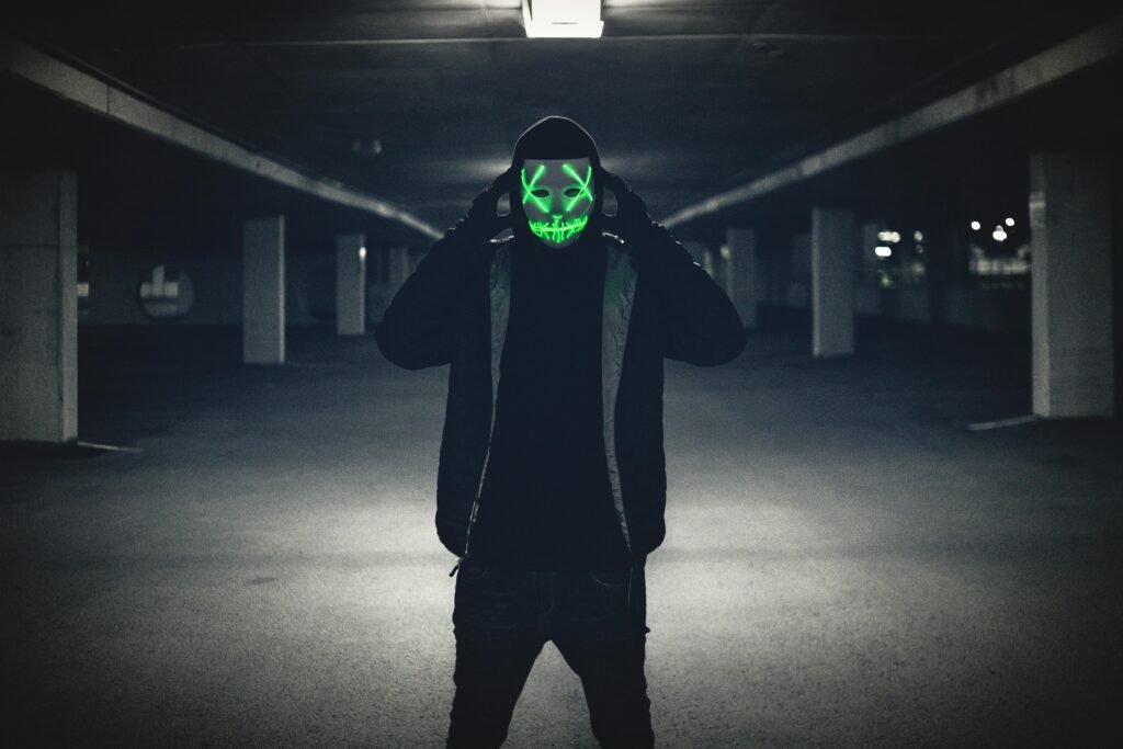 A person wearing a neon LED mask stands in a dimly lit underground parking lot, creating an eerie atmosphere.